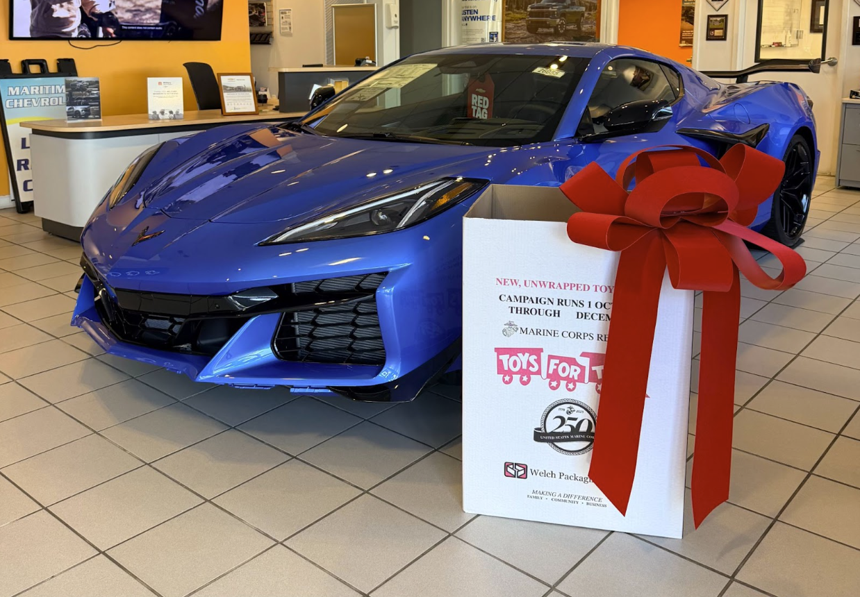 toys for tots box with giant bow in front of blue corvette model