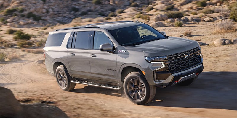 2024 Chevrolet Suburban parked on a dirt road, showcasing its rugged design and off-road capabilities.