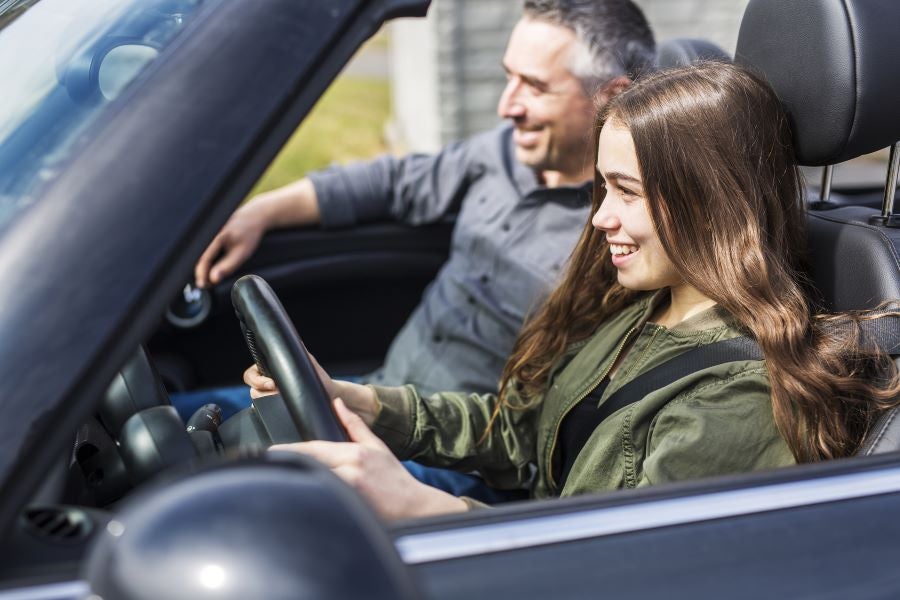 Teen smiling and driving a car.